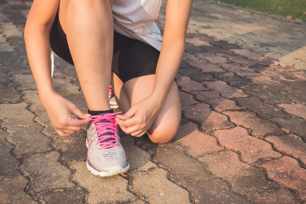 woman-lacing-up-her-gray-and-pink-nike-low-top-athletic-shoe-601177 Adult woman tying pink laces on running shoes outdoors. Focuses on fitness and lifestyle.
